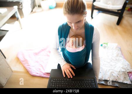 Mother holding small baby, putting her in baby sling, wrap. Unconditional paternal love, mother's Day. Stock Photo