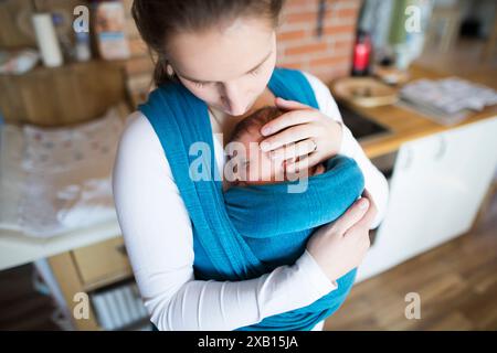 Mother holding small baby, putting her in baby sling, wrap. Unconditional paternal love, mother's Day. Stock Photo