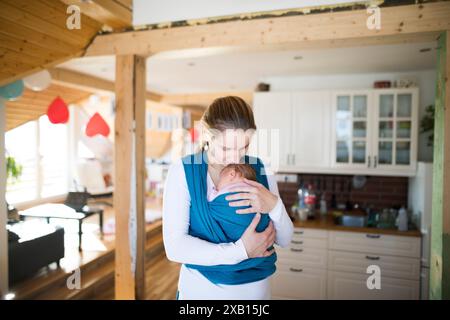 Mother holding small baby, putting her in baby sling, wrap. Unconditional paternal love, mother's Day. Stock Photo