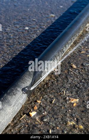 Leaking black polyethylene water pipe on ground outdoors Stock Photo