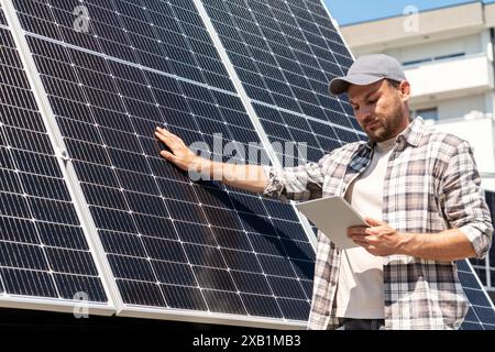 Technician of solar plant checks the maintenance of solar panels in city, touching solar panel surface and looking at the digital tablet. Stock Photo