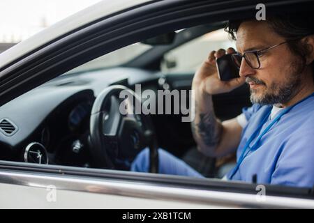 Doctor getting into car, going home from work, phone calling. Work-life balance of healthcare worker. Stock Photo
