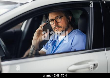 Doctor getting into car, going home from work, phone calling. Work-life balance of healthcare worker. Stock Photo