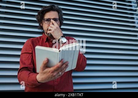 Portrait of mature businessman standing on city street, reading book. Handsome man with glasses in suit. Stock Photo