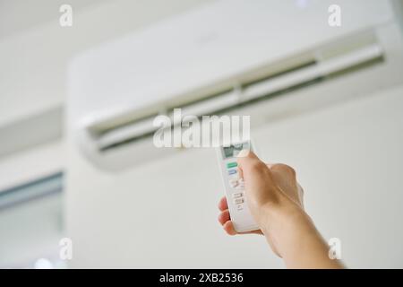 Adjusting air conditioner temperature with remote control. Hand holds remote control and setting comfortable temperature on climate system in apartmen Stock Photo