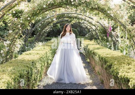 Joyful women walking in garden under flowers in slate blue dress Stock Photo