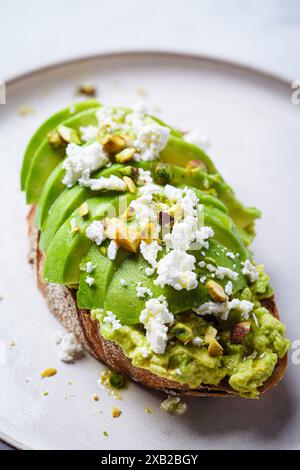 Avocado toast with feta and pistachio on a plate, white marble background. Stock Photo