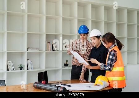 Team of Engineers and Architects Collaborating on Construction Project in Modern Office with Shelves in Background Stock Photo