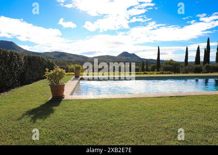 A scenic view of a swimming pool surrounded by lush greenery and potted plants, with rolling hills and mountains in the background. The serene landsca Stock Photo