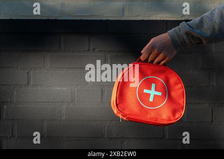 A hand holding first aid kit bag for emergency situations. A red first aid kit with a white cross isolated Stock Photo