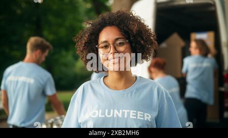 Portrait of a Happy Helpful Black Female Volunteer. Young Adult Multiethnic Latina with Afro Hair, Wearing Glasses, Smiling, Posing for Camera. Humanitarian Aid and Volunteering Concept. Stock Photo