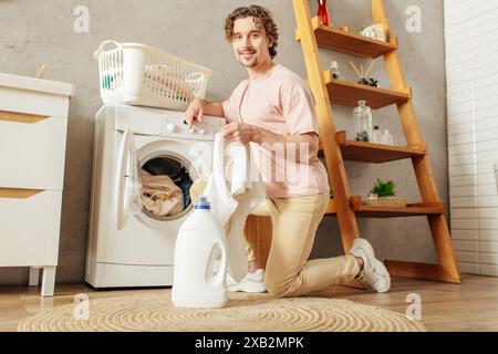 A handsome man in a pink shirt meticulously doing laundry at home. Stock Photo