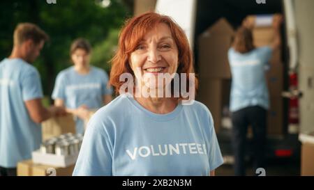 Portrait of a Happy Helpful Middle Aged Female Volunteer. Adult Caucasian Woman in Blue T-Shirt, Smiling, Looking at Camera. Humanitarian Aid, Donations Center and Volunteering Concept. Stock Photo