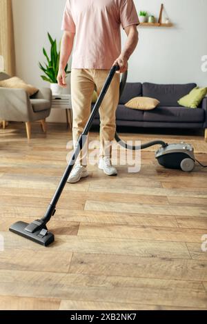 A man in cozy homewear uses a vacuum to clean a wooden floor. Stock Photo