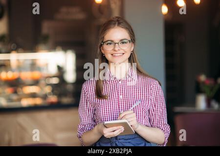 Portrait of a beautiful friendly waitress in glasses with notepapers and pen ready to take your order Stock Photo