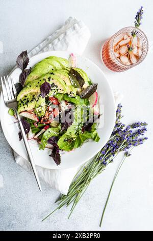 Fresh garden salad with mixed greens, avocado slices, cucumbers, tomatoes, radishes, olives, sesame seeds, and a side of lavender. Stock Photo