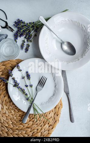 An inviting summer table setting featuring elegant white dishes, silverware, and fresh lavender flowers on a woven placemat Stock Photo