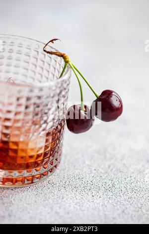 A close-up image of a glass filled with gourmet cherry liqueur, accompanied by ripe cherries draping gracefully over the rim Stock Photo