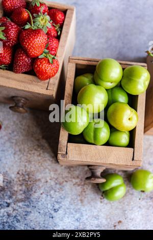 Organic ripe strawberries, sweet cherries, and green plums arranged in vintage wooden boxes on a textured surface, showcasing nature's colorful bounty Stock Photo