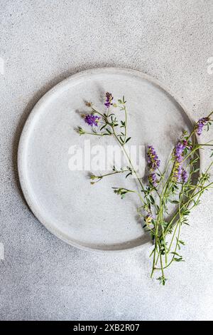 Top view of a minimalist summer table setting featuring a ceramic plate and delicate purple wildflowers, creating an elegant yet simple design. Stock Photo