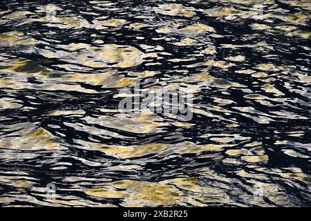 A photo capturing intricate ripples and reflection patterns on a dark, textured water surface of Cantabria, Spain, highlighted by subtle gold tones Stock Photo