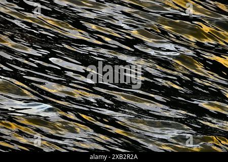 This image captures the dynamic movement of waves with striking reflections of golden and black hues, creating a mesmerizing abstract pattern on water Stock Photo