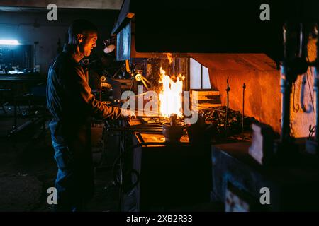 A male blacksmith working with intense fire in his forge, heating up metal surrounded by traditional tools. Stock Photo