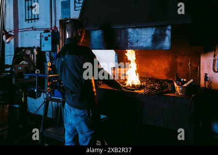 Blacksmith working with metal at fiery forge in traditional workshop Stock Photo
