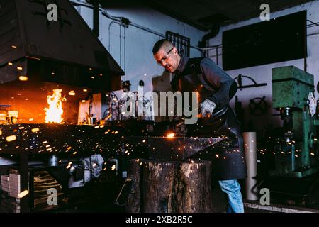 A skilled male blacksmith forges with intense heat, sending sparks flying in all directions. Stock Photo