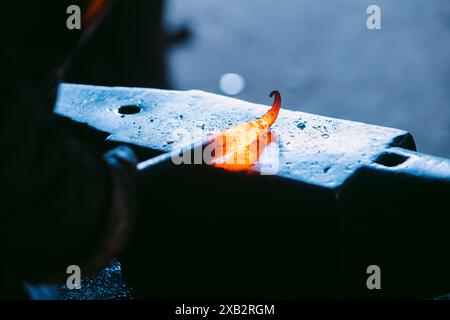 Close-up of incandescent iron being shaped on an anvil by an unrecognizable blacksmith, with a focus on the glowing metal and the tools used. Stock Photo