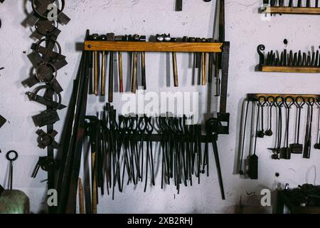 A variety of vintage blacksmithing tools neatly organized on a white wall within a craftsman's workshop. Stock Photo
