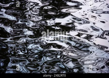 This image captures the intricate patterns and abstract shapes formed by light reflections on the ocean surface, all depicted in a dramatic monochrome Stock Photo