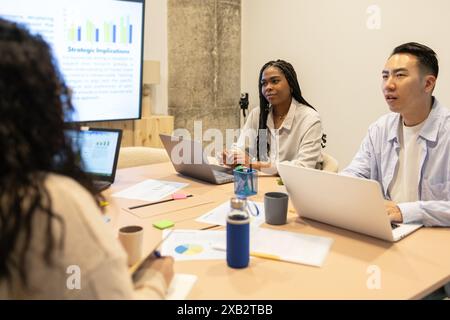 A team of diverse friends engage in a collaborative work session in a coworking space, focusing on a presentation and discussing strategic implication Stock Photo