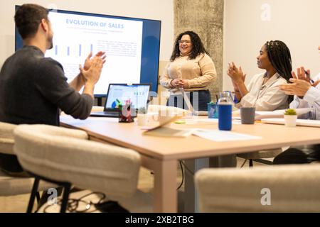 A diverse team of colleagues collaborates in a coworking space, applauding a presentation about sales evolution Stock Photo
