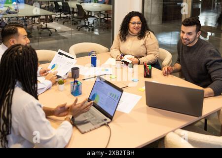 Diverse group of friends collaborating on a project in a modern coworking space with laptops and documents on the table Stock Photo
