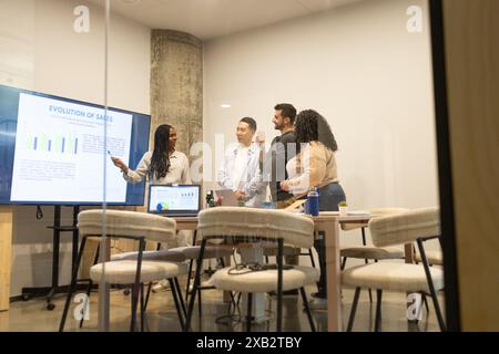 A diverse group of friends works together in a modern coworking environment, engaging in a business discussion with sales data on the screen Stock Photo