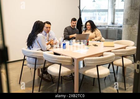 A diverse group of friends engaged in a collaborative work session at a well-lit coworking table, focusing on a project with a laptop and notes Stock Photo