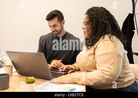 Two friends engaging in a productive team session at a coworking desk, sharing ideas for a project with a laptop and documents Stock Photo
