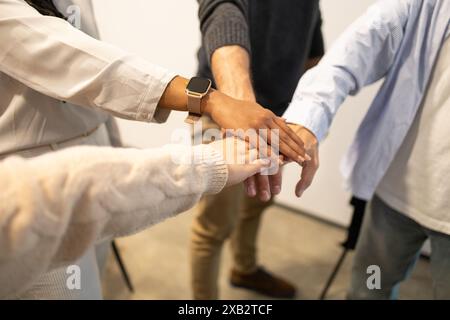 Diverse group of friends stacking hands together, showcasing teamwork in a coworking environment Stock Photo