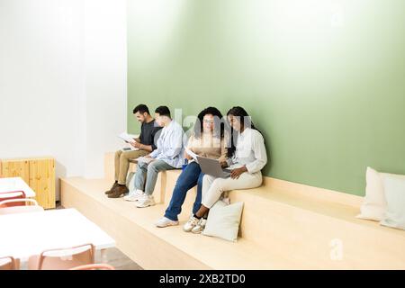 A multi-ethnic group of friends or colleagues work side by side on a tiered seating in a bright, contemporary coworking environment Stock Photo