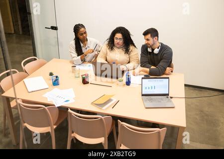 A multiracial group of friends or colleagues engaging in teamwork at a bright coworking environment, with laptops and documents on the table Stock Photo
