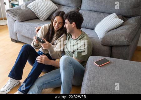 A young couple relaxes in a cozy living room, smiling while playing with a video game controller The setting promotes a casual, fun home lifestyle Stock Photo