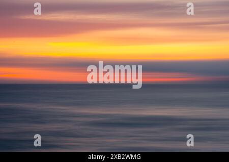 A serene, abstract view capturing the blurred motion of a sunset's warm hues over the ocean at Atlanterra Beach. Stock Photo