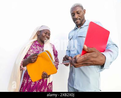 Two colleagues holding folders and a digital tablet share a joyful moment during an outdoor summer breakfast meeting, implying a productive start to t Stock Photo