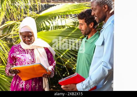 Three individuals engaging in a professional discussion outdoors, surrounded by lush green palm fronds, symbolizing a summer breakfast meeting infused Stock Photo