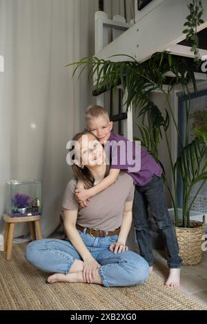 A smiling mother and her child enjoy a quiet moment beside a home aquarium, embracing family time and aquatic life behind them. Stock Photo