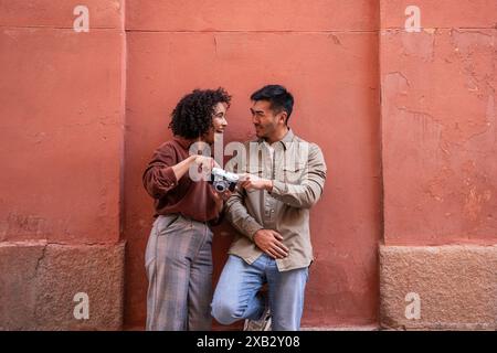 A cheerful multiracial couple in Madrid, Spain, enjoys their time together. The Chinese man and Hispanic woman are smiling and holding a vintage camer Stock Photo