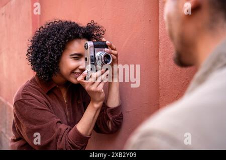 A multiethnic couple enjoys their time in Madrid, Spain. The Hispanic woman is capturing a moment with a vintage camera while the Chinese man stands n Stock Photo