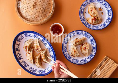 A vibrant image showcasing steamed Chinese dumplings, drizzled with spicy sauce and sesame seeds, elegantly plated on blue and white porcelain dishes Stock Photo