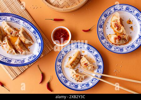 A vibrant top-view of traditional Asian dumplings on ornate blue and white plates, accompanied by a spicy dipping sauce and chili peppers on a burnt-o Stock Photo